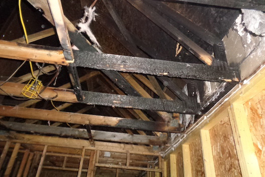 Internal view of fire-damaged, blackened wooden roof trusses.