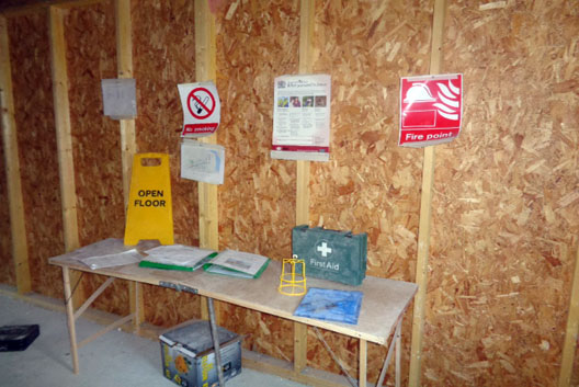 First aid station on trestle table against temporary wooden wall accompanied by safety signage.