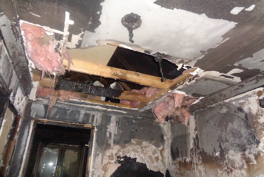 Internal view of fire-damaged ceiling with holes, exposed beams and cables dangling.