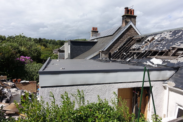 External view of property with partially damaged roof with exposed beams; debris can be seen piled in the garden. House Fire Insurance Reinstatement Lanark