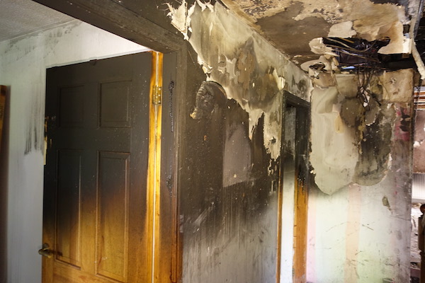 Internal view of fire-damaged ceiling and door; both are discoloured and the ceiling is scorched. Cables are hanging from the ceiling. House Fire Insurance Reinstatement Lanark