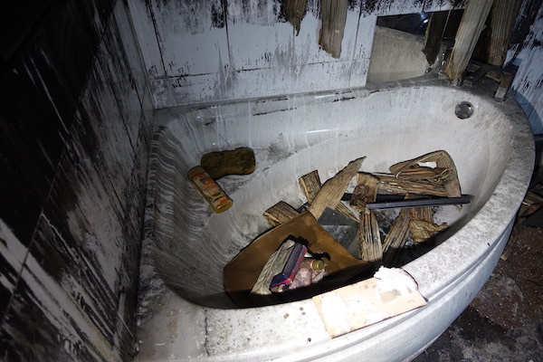 Internal view of fire-damaged corner bath with discoloured walls and debris in the bath itself. House Fire Insurance Reinstatement Lanark