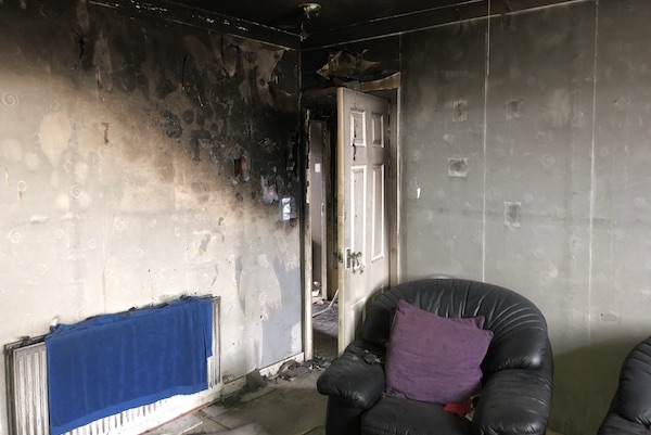 Fire damaged living room with blackened walls and damaged door at house in Cumnock. case study House Fire Damage Insurance Restoration Cumnock