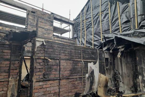 External view of a house that has suffered fire damage featuring exposed blackened brickwork, bare ceiling, protective plastic sheets and scaffolding.