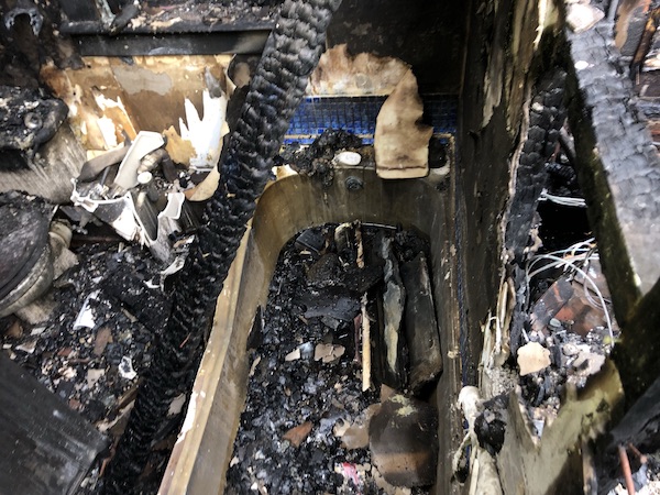 Bird's eye view of fire-damaged bath with blackened walls and surfaces, with debris all over the room and surrounding area.
