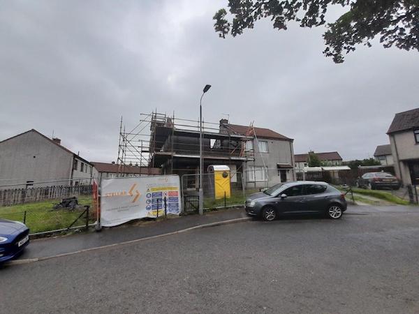 External view of house with scaffolding around it, portable toilet outside in garden and Stellar insurance reinstatement services banner on safety fence.