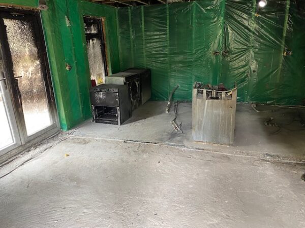 Internal view of fire-damaged room with green plastic sheeting on the walls, scorched window and French doors and damaged appliances. House Fire Insurance Reinstatement Lanark
